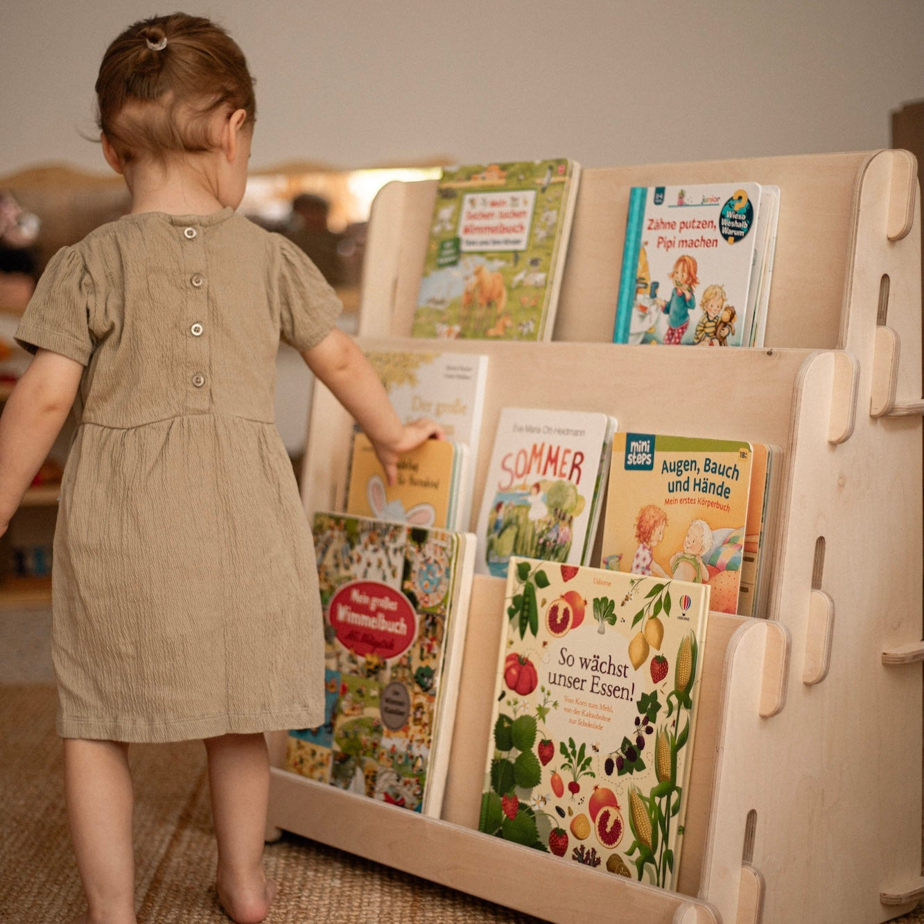 Kleinkind steht vor Montessori Bücherregal und greift nach einem Buch