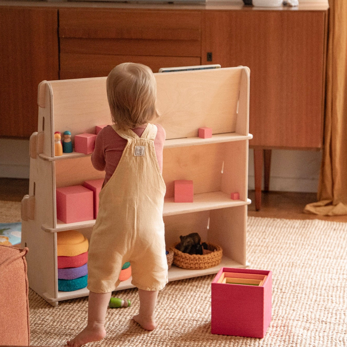 Kind nimmt Spielzeug aus Rückseite des Montessori Bücherregals